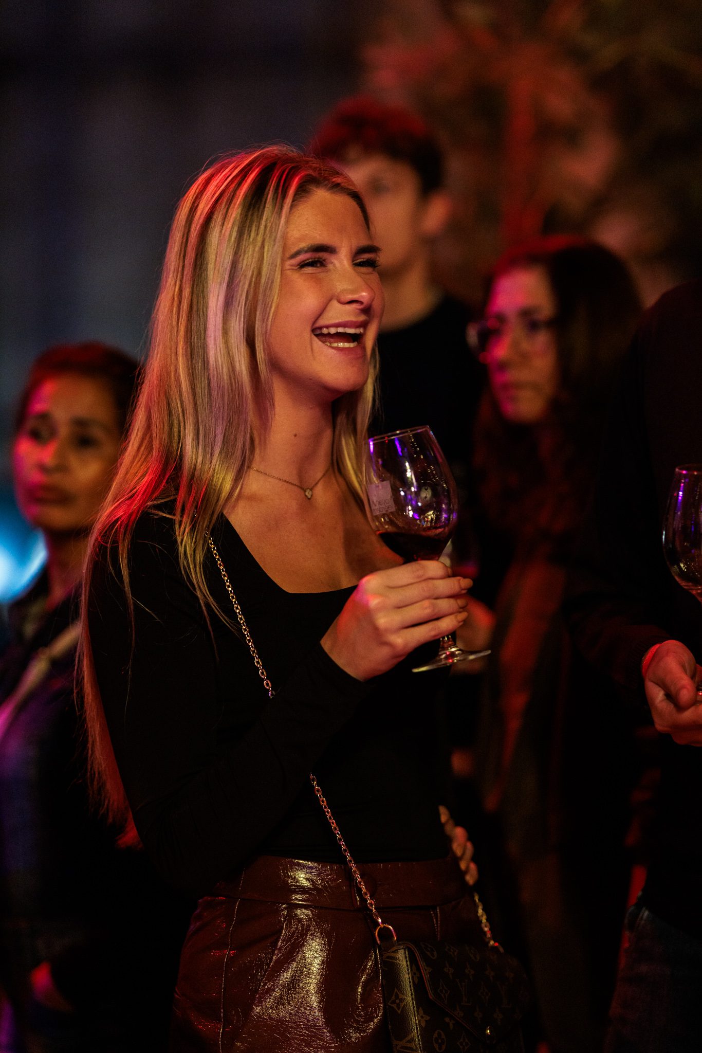 Vrouw proeft lachend een glas rode wijn te midden van andere bezoekers op een festival
